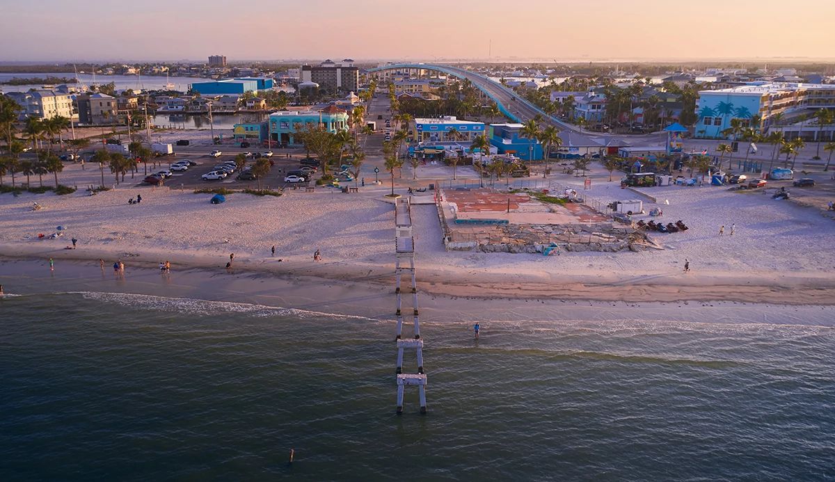 Aerial view of a beach, damaged pier, and curved highway