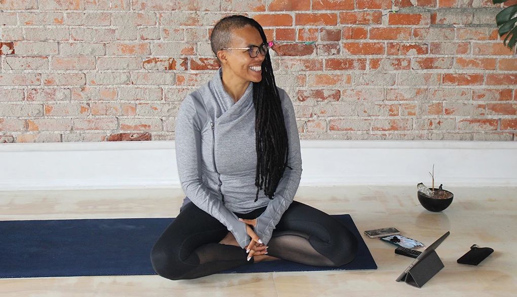 A woman, Ali Duncan, smiling and sitting on a mat in a yoga studio