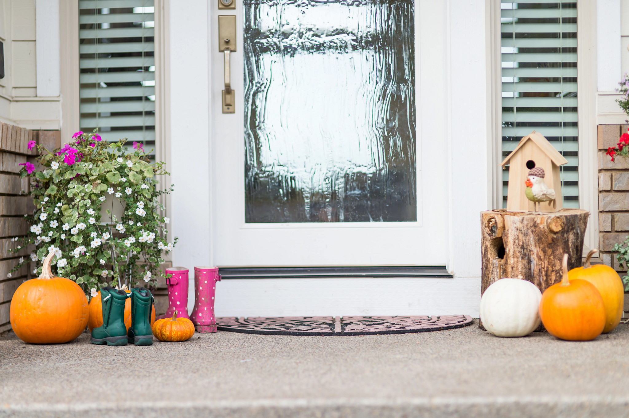 Several pumpkins sit on the front porch, surrrounded by flowers and boots.