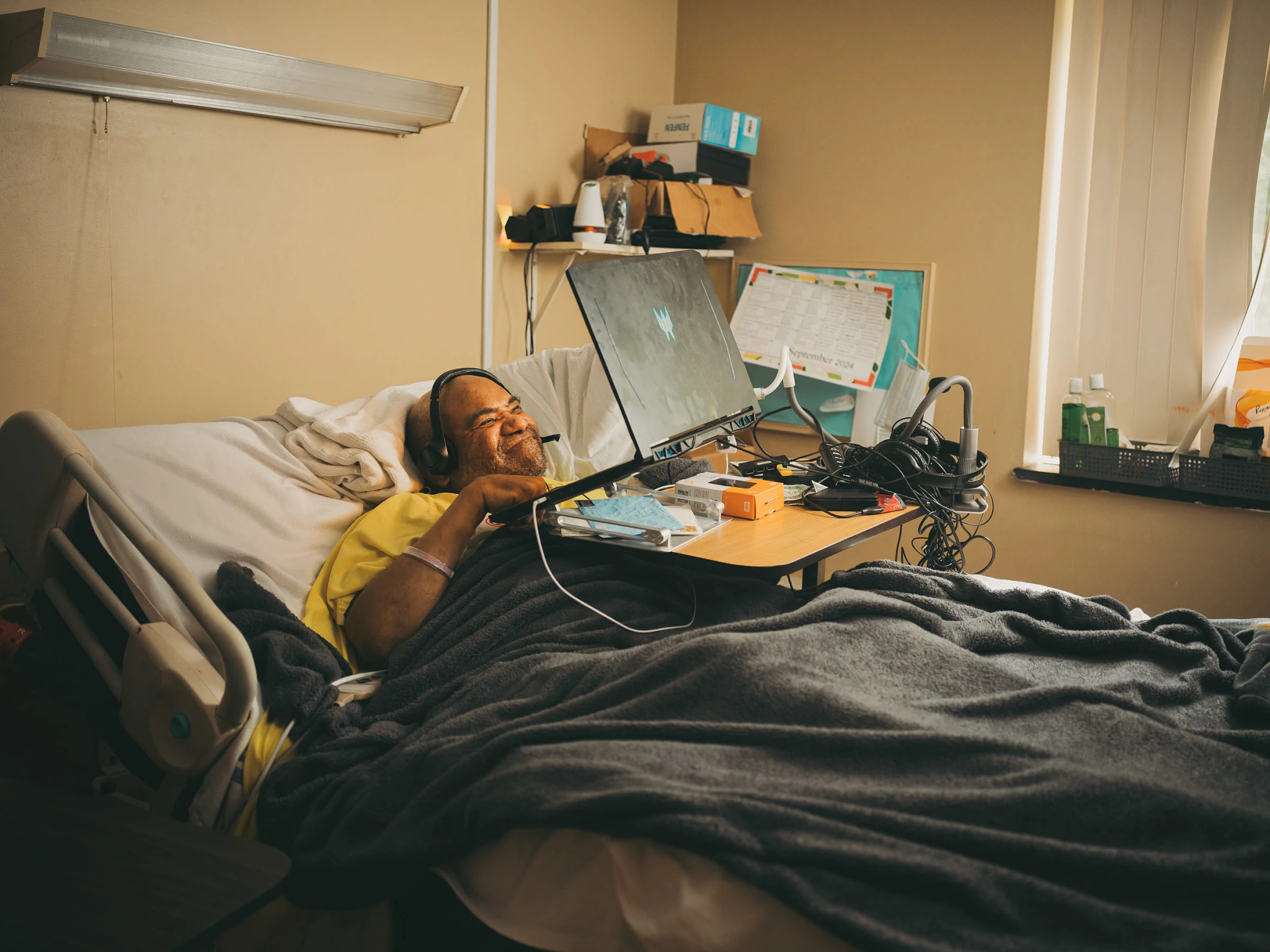 maurice miller, wearing a headset, smiles at his laptop while laying in bed