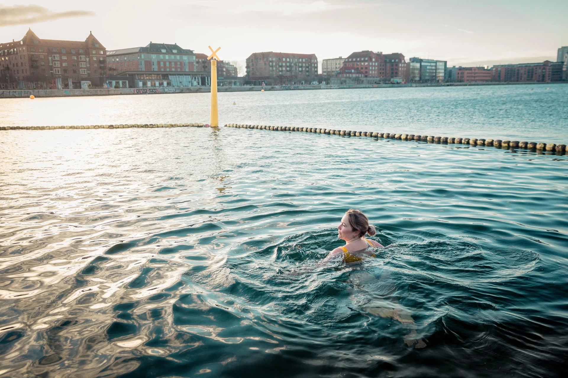 a woman swimming in water with buildings in the background in denmark