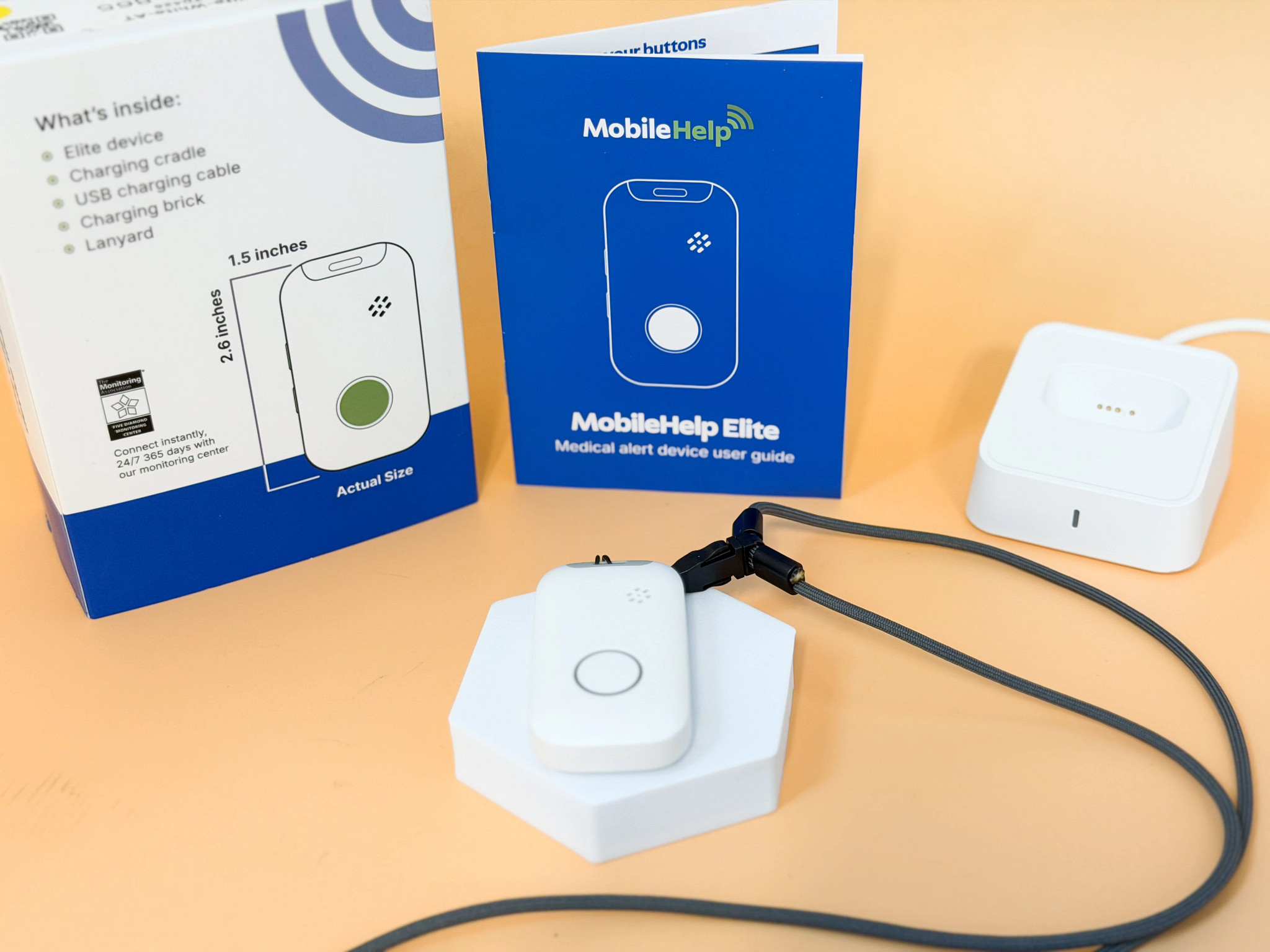 The MobileHelp Elite medical alert device displayed in front of the charging dock and packaging.