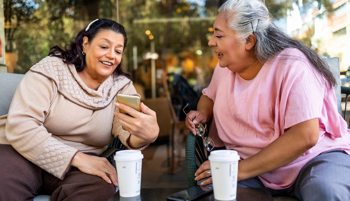 Two women at a coffee shop smiling and sharing photos on their phones