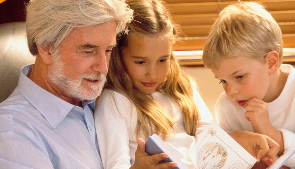 Grandfather with hearing loss reading a book out loud to his grandchildren sitting on his lap