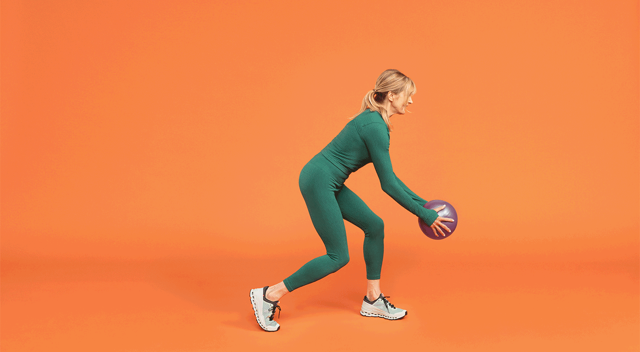 Person in green athletic wear performing a core-strengthening exercise with a medicine ball against an orange background