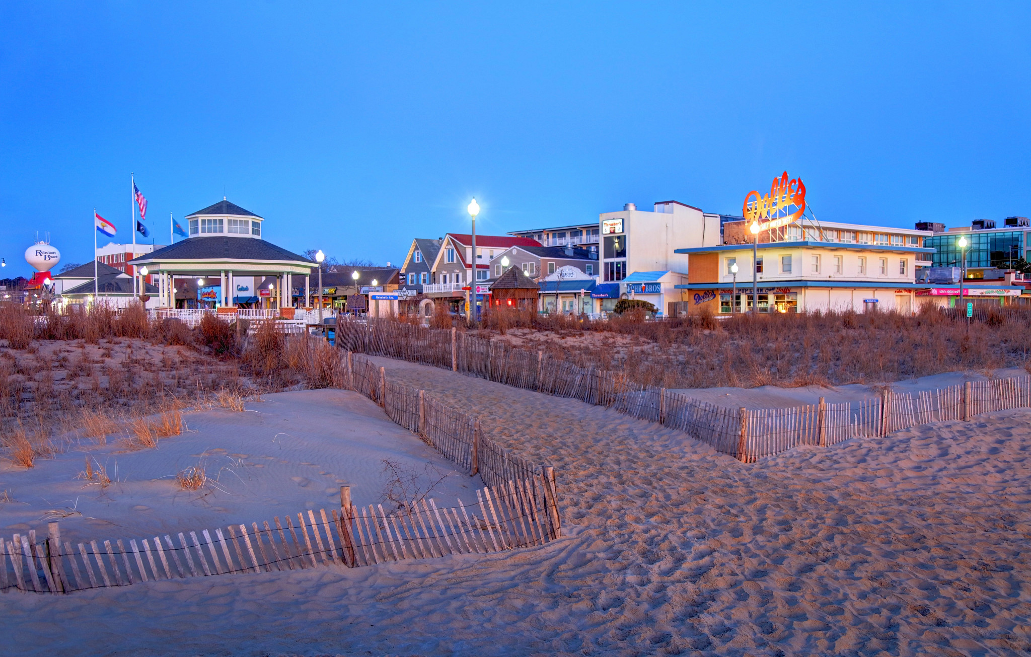 a beach in the foreground with a gazebo and stores in the background