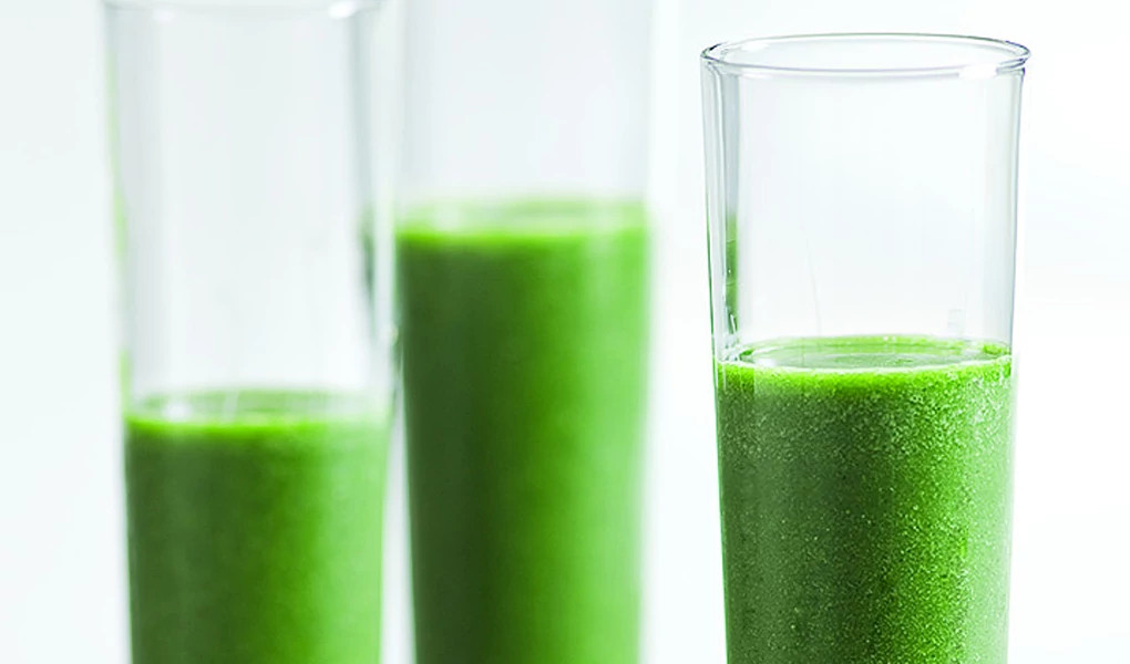 A close-up view of three glasses of green smoothie