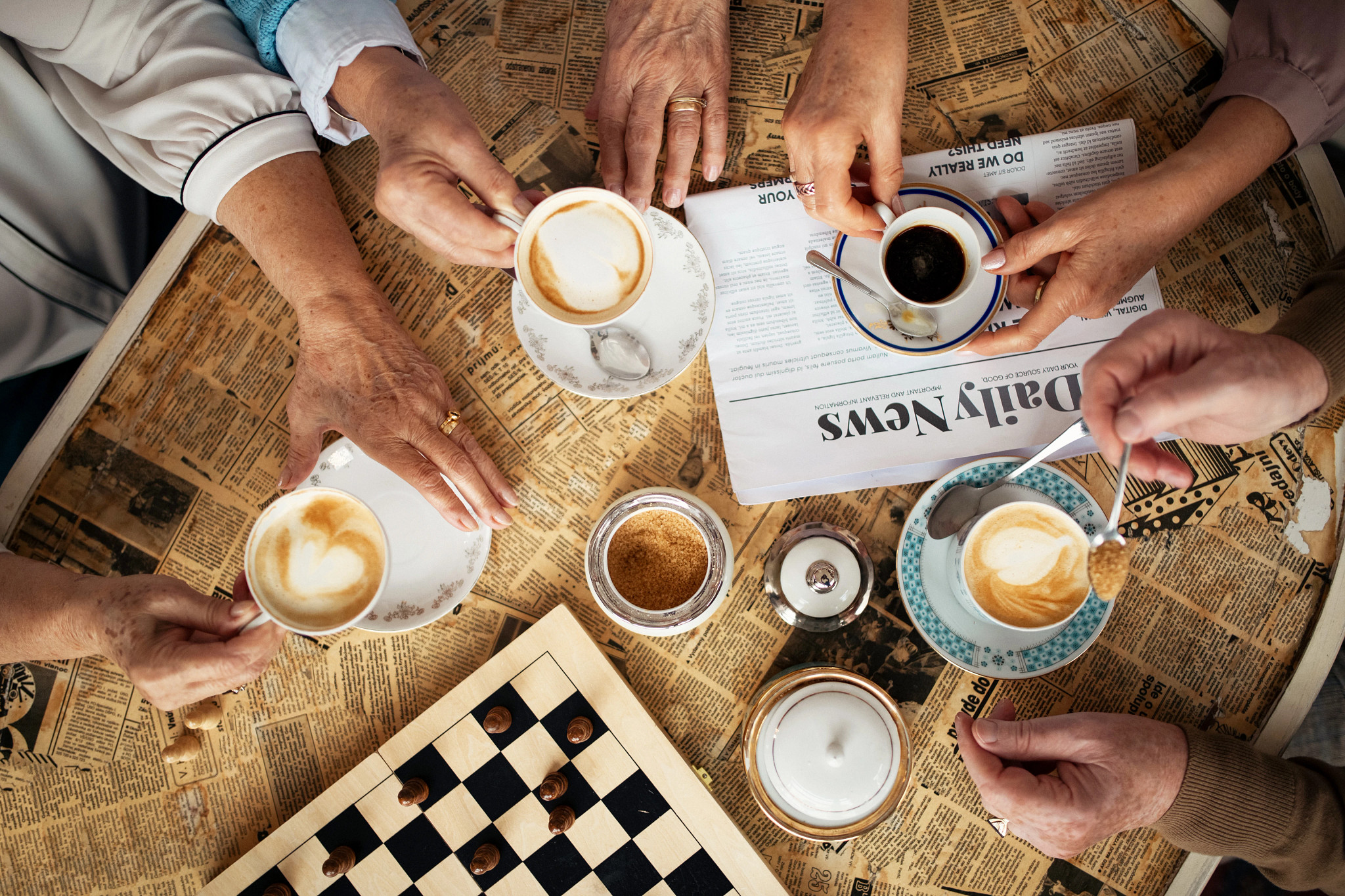 A group of people enjoy cups of coffee on a newspaper-themed coffee table