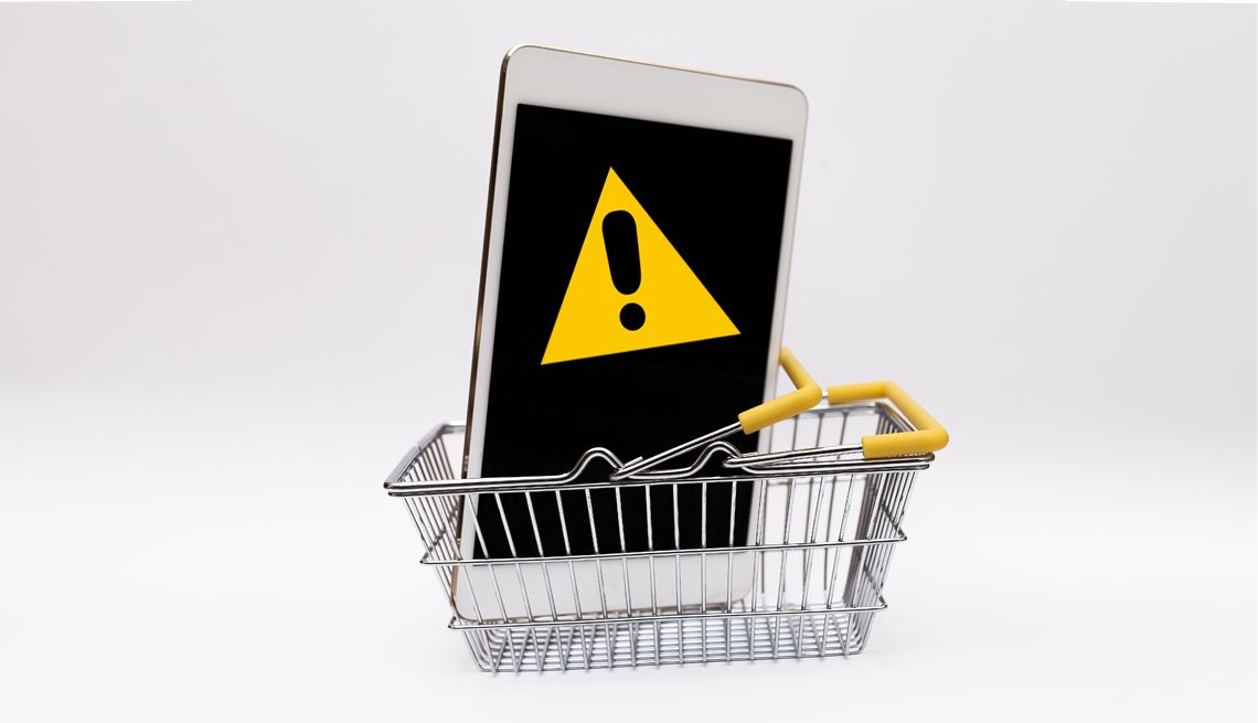 How to Spot Online Shopping Scams a shopping cart with a phone that has a yellow sign on it with an exclamation point