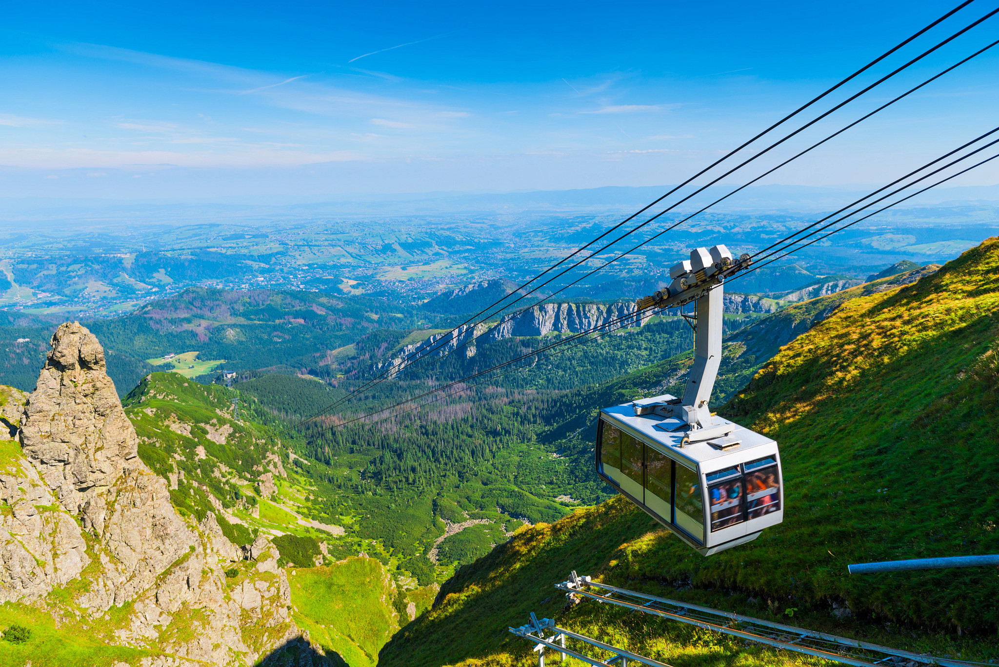 Cable car traveling above a scenic mountain valley with panoramic views of forests, peaks, and open landscapes.