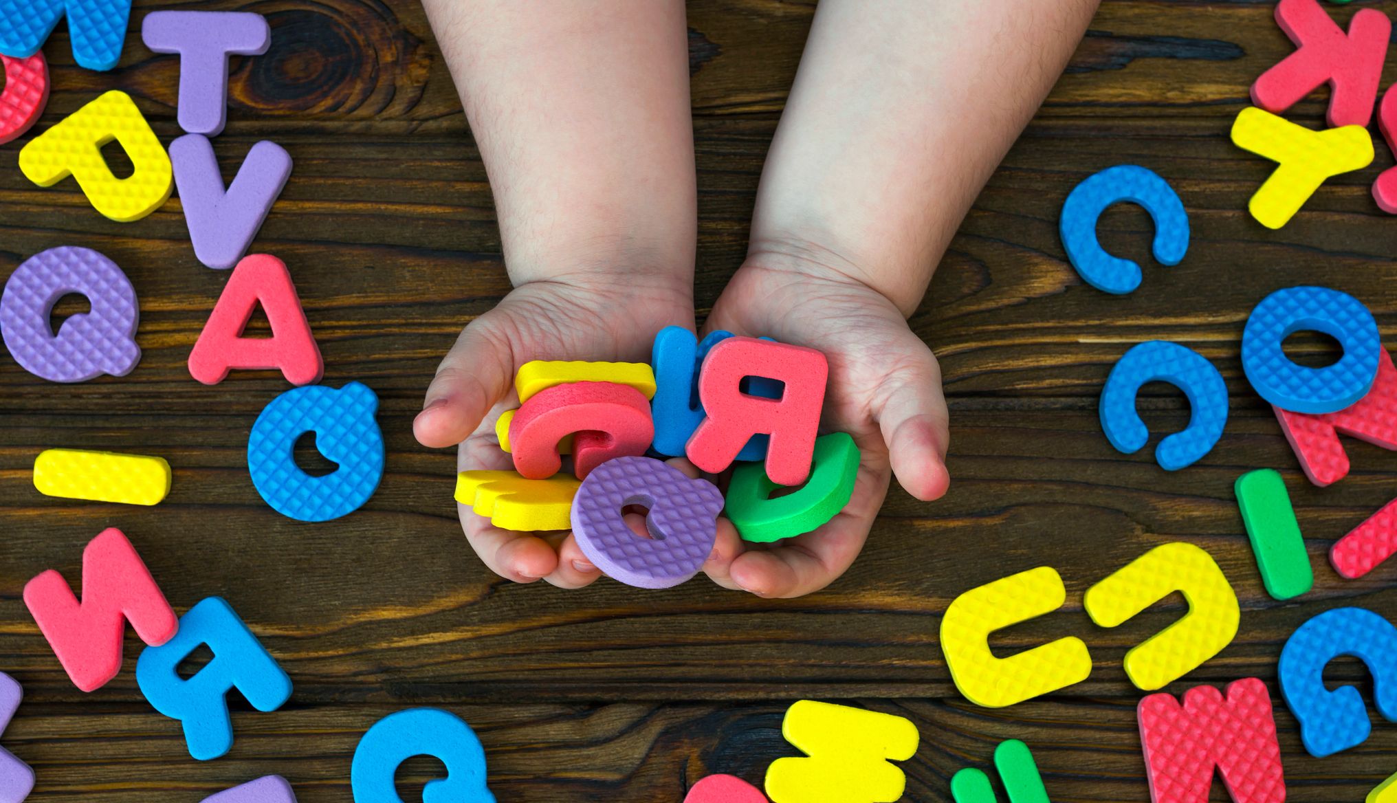 letras del alfabeto inglés en las manos de un bebé sobre fondo de madera