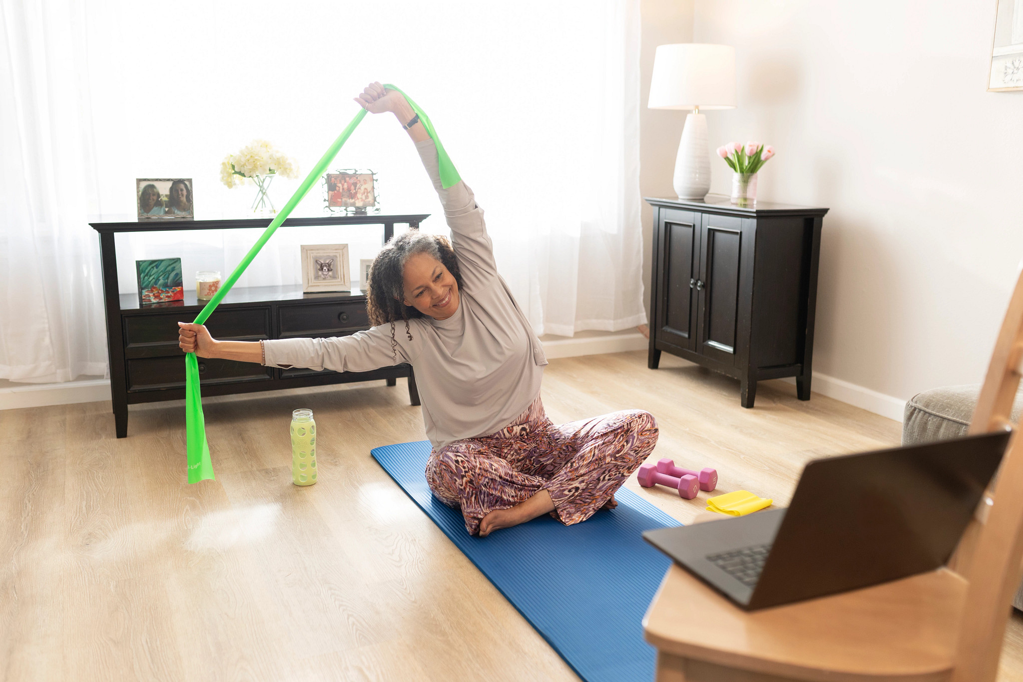 A participant follows a virtual fitness class while performing a resistance band stretch designed to improve flexibility and mobility. Pictured in photo: Veronica Senseri CREDIT: Photograph by Bill Zelman for AARP.