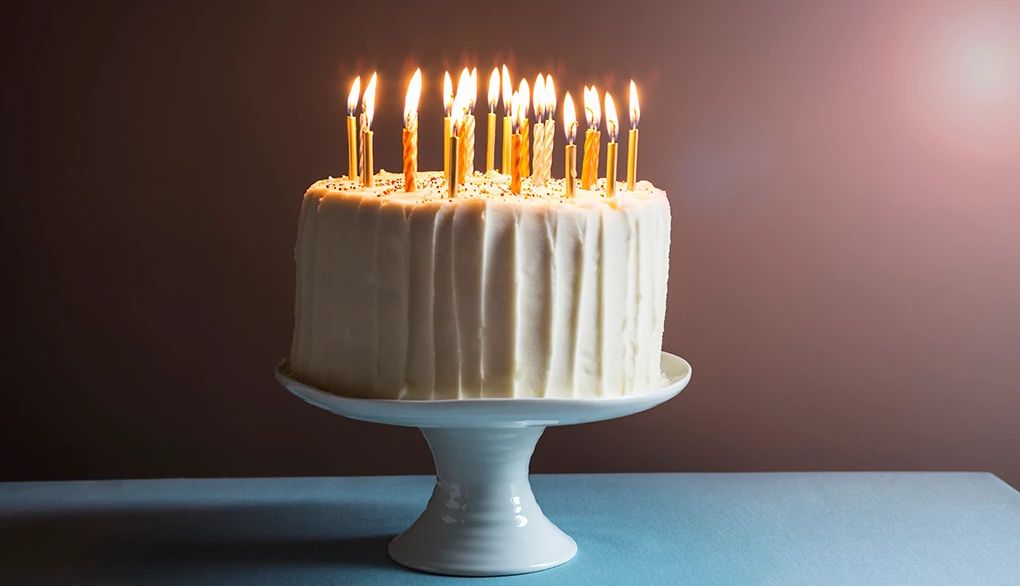 Remembering birthdays can sometimes be a challenge A white birthday cake with candles on a stand against a dark background