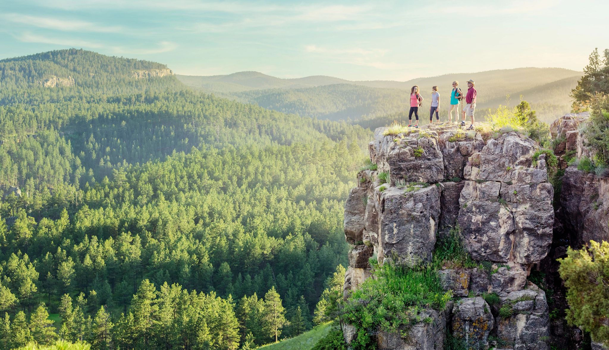 Multigenerational Trips people on a cliff looking out at mountains and trees below