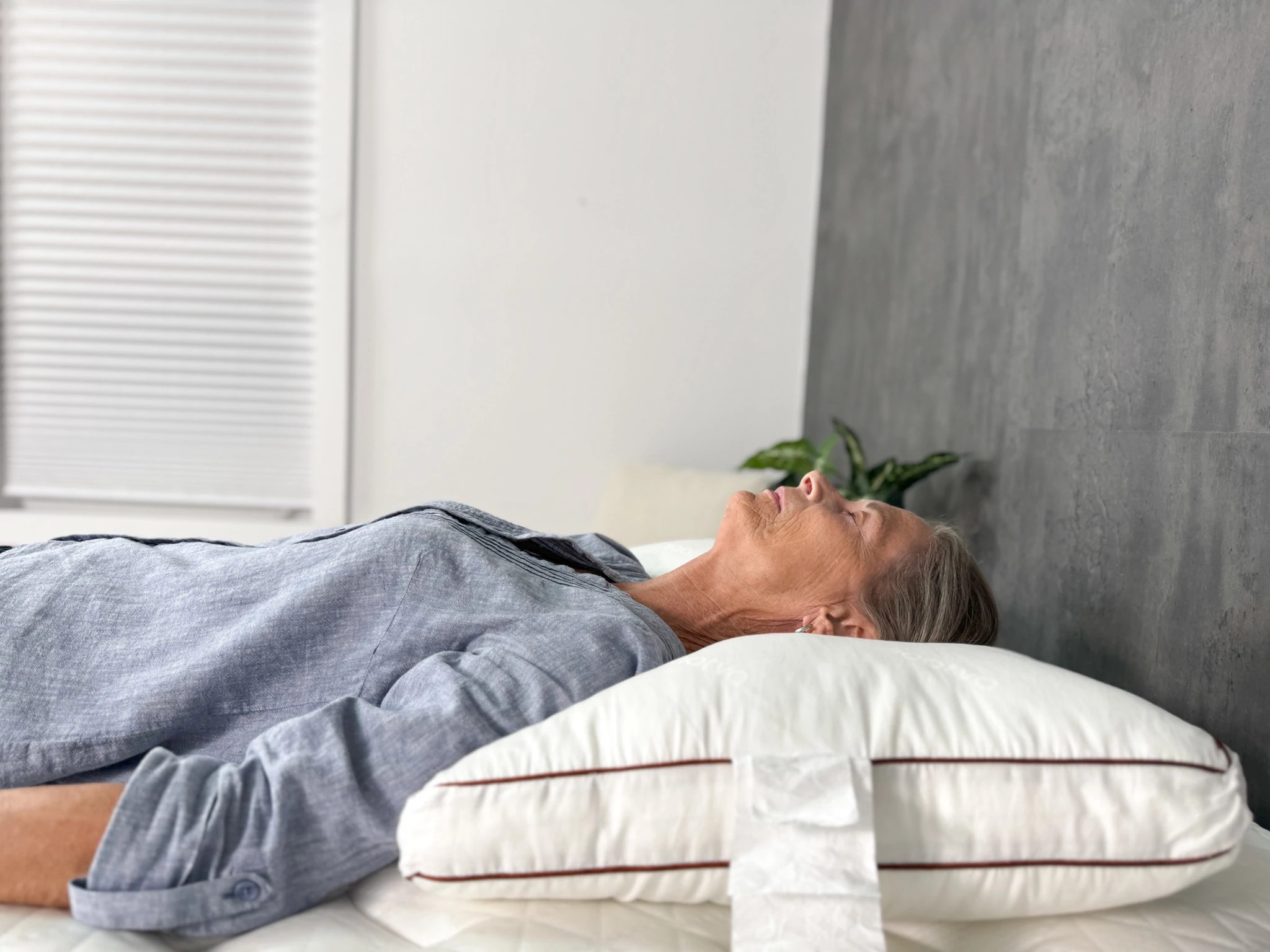 An older woman lying on her back with her head resting on the Saatva Latex Pillow