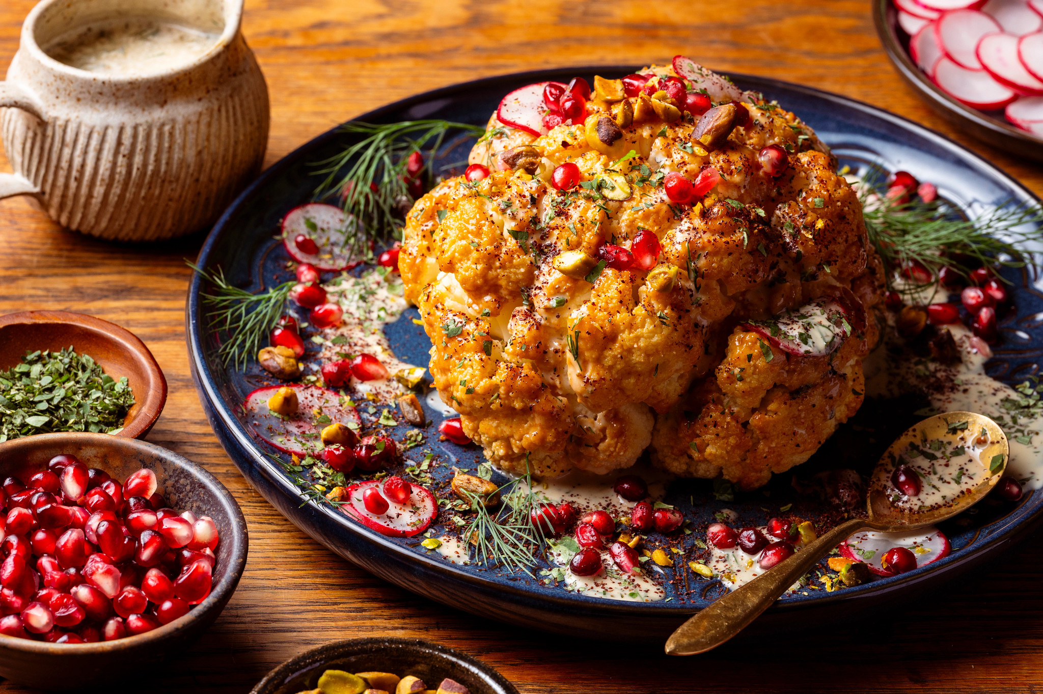 Large head of cauliflower with pomegranate seeds and drizzling sauce.