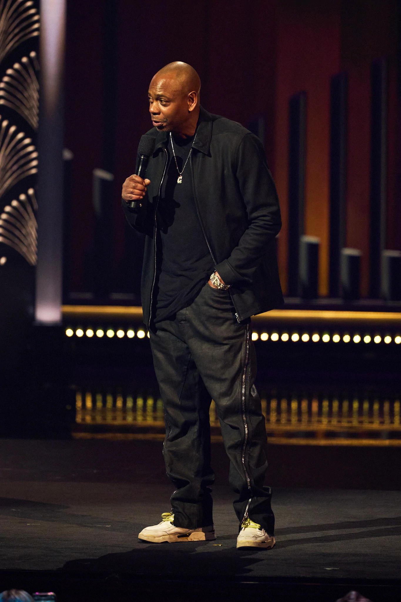 Dave Chappelle speaking into a microphone onstage at the 25th Annual Mark Twain Prize For American Humor