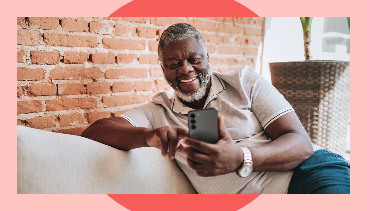 A man smiles while sitting down and scrolling on his cell phone