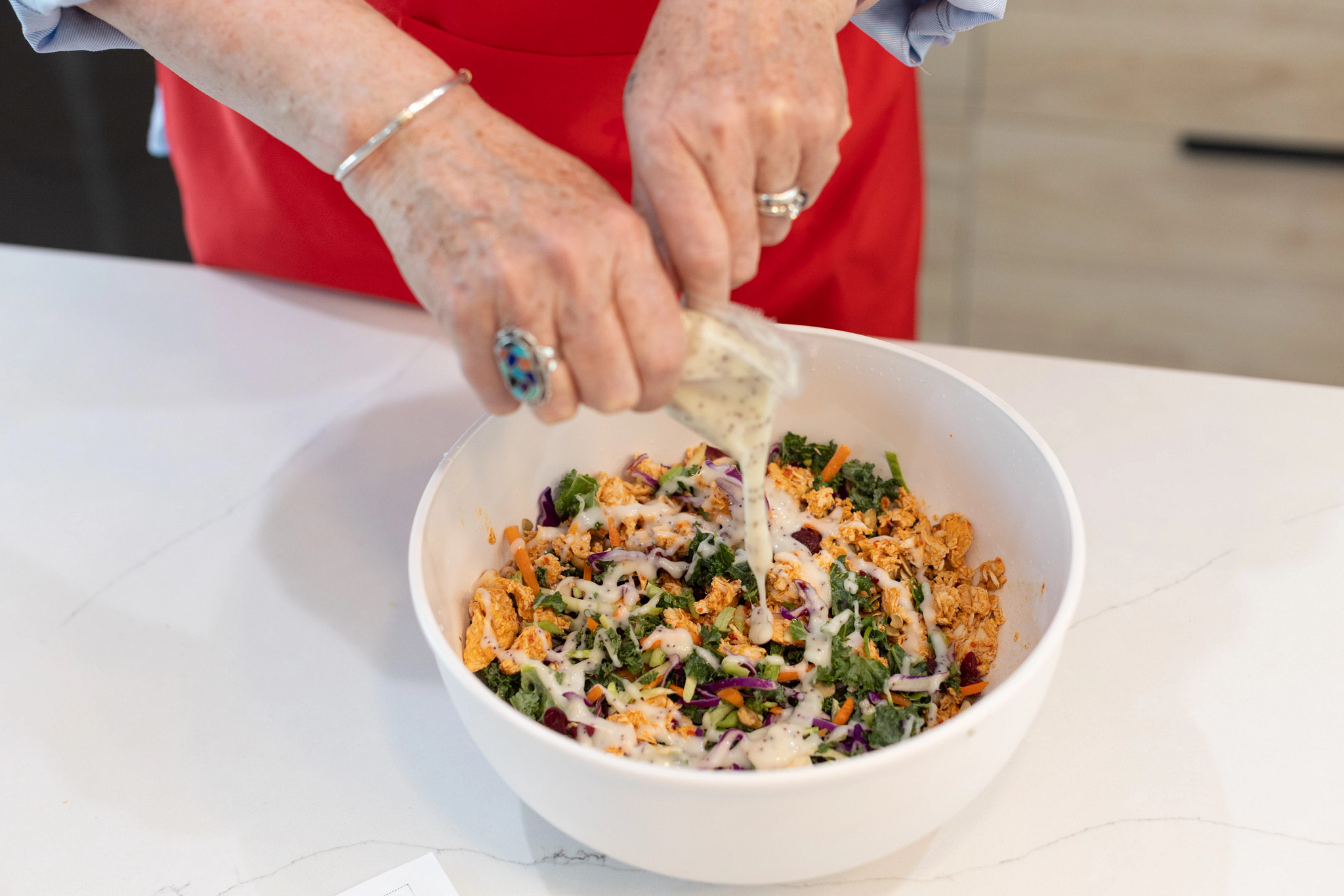 A person squeezing dressing onto the Hungryroot chicken kale salad meal in a bowl