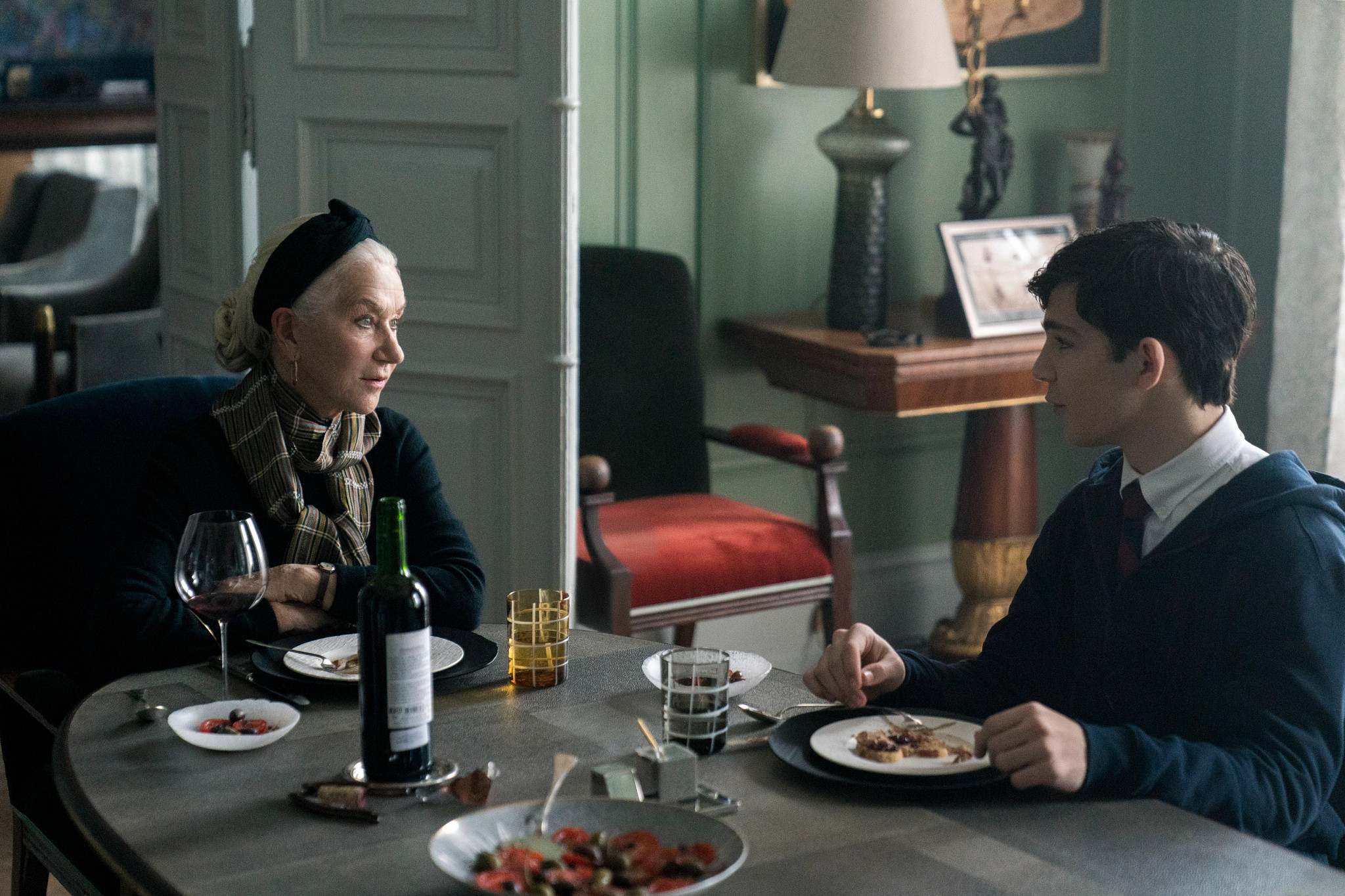 Helen Mirren as Grandmère and Bryce Gheisar as Julian sitting at a table with food and wine in front of them in a still from White Bird A Wonder Story