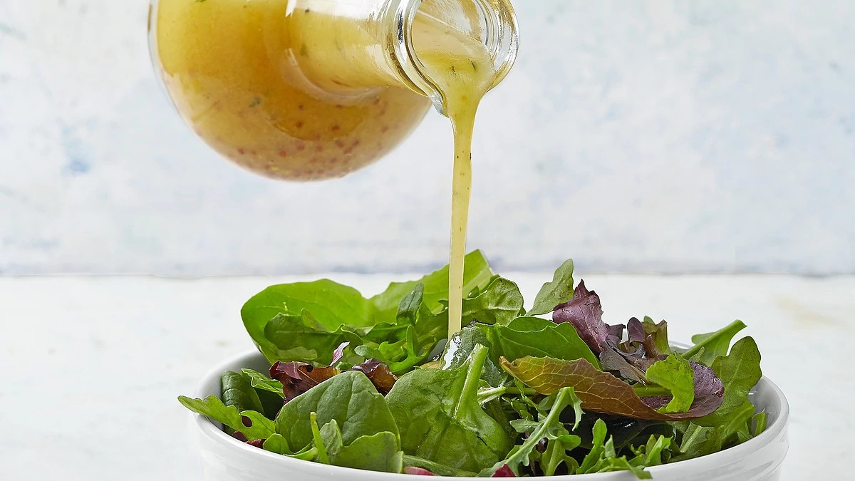 A close-up view of basic green salad with vinaigrette being poured onto the salad in a bowl