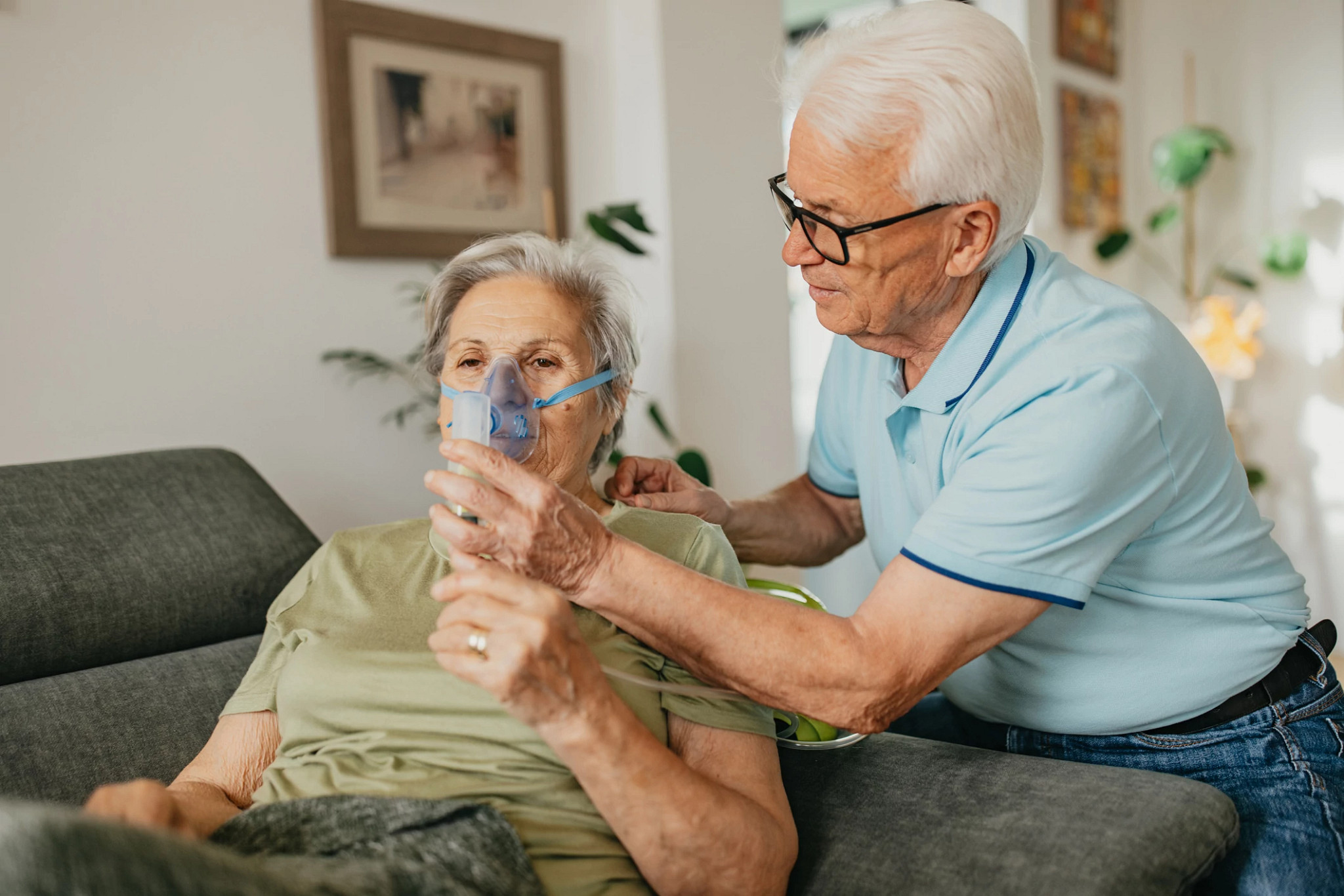 Senior man assisting senior woman during process of medical inhalation
