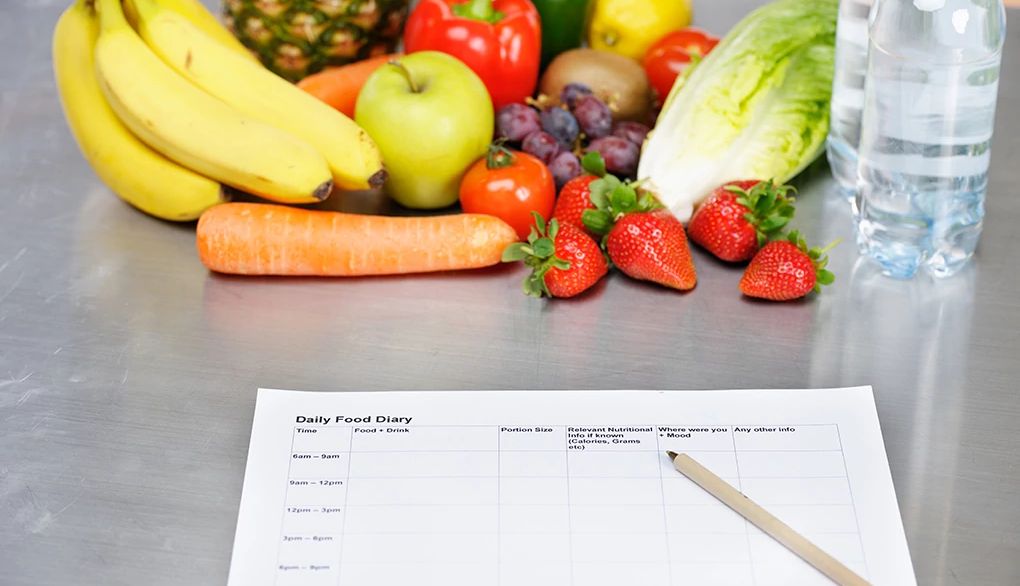 Understanding your food cravings can help you make healthier choices A daily food diary paper next to fruits and vegetables