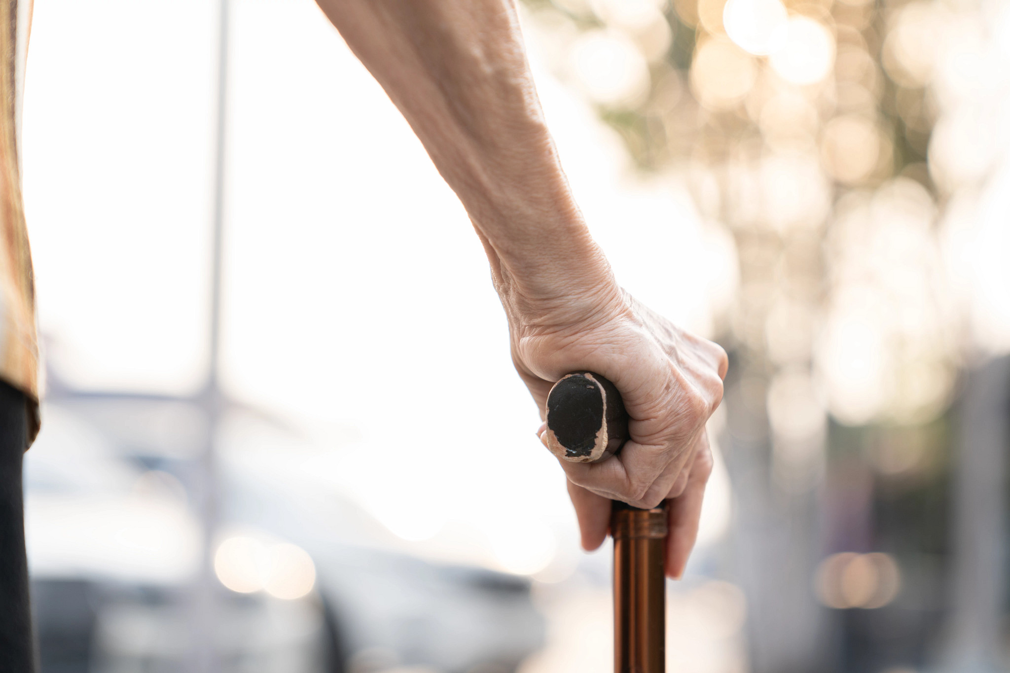 Close-up of an elderly person's hand holding a cane while walking outdoors