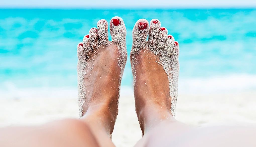 Vacations may help you manage your stress Two sandy feet of a person lying on the beach