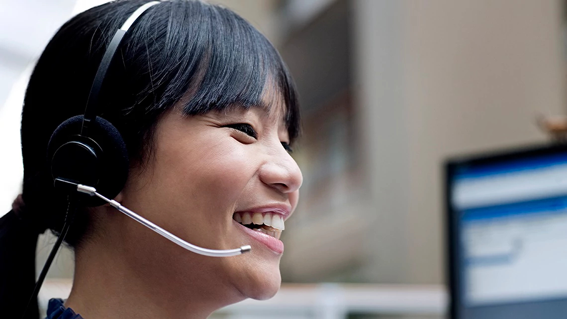 Woman with black hair and bangs smiling with phone headset on