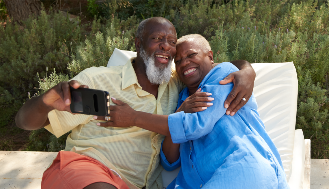 Couple sitting on patio furniture looking at phone together and laughing