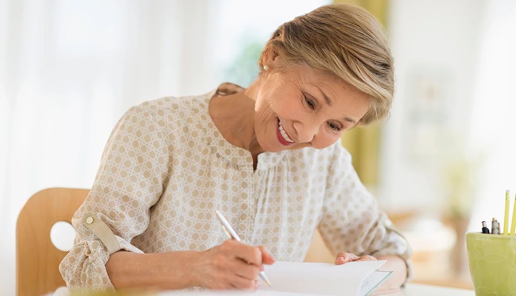 Paying attention to the positive may ease stress A woman smiling and writing in a journal