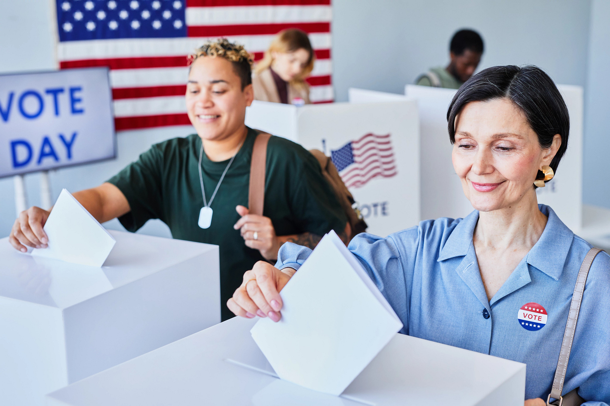 Portrait of two smiling American women voting and putting ballots in bins on election day