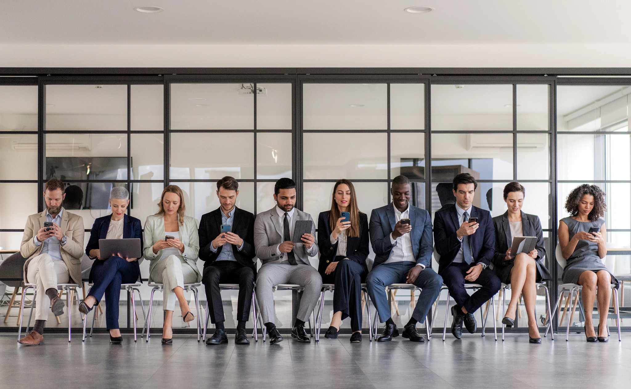 a line of people sitting in chairs all looking at their mobile devices