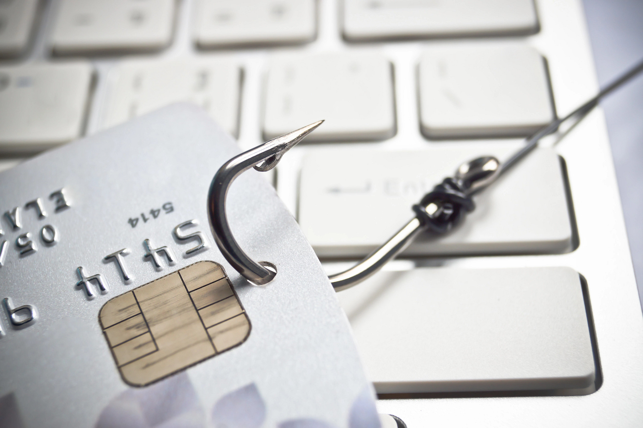 A credit card with a fish hook through it symbolizing how scammers steal money and personal information. A computer keyboard is in the background.