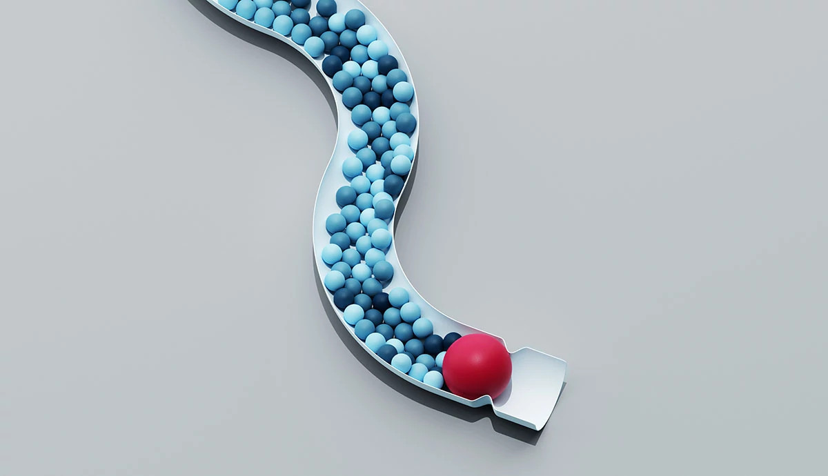 3D illustration of a winding white tube filled with small blue spheres that are blocked by one large red sphere at the end