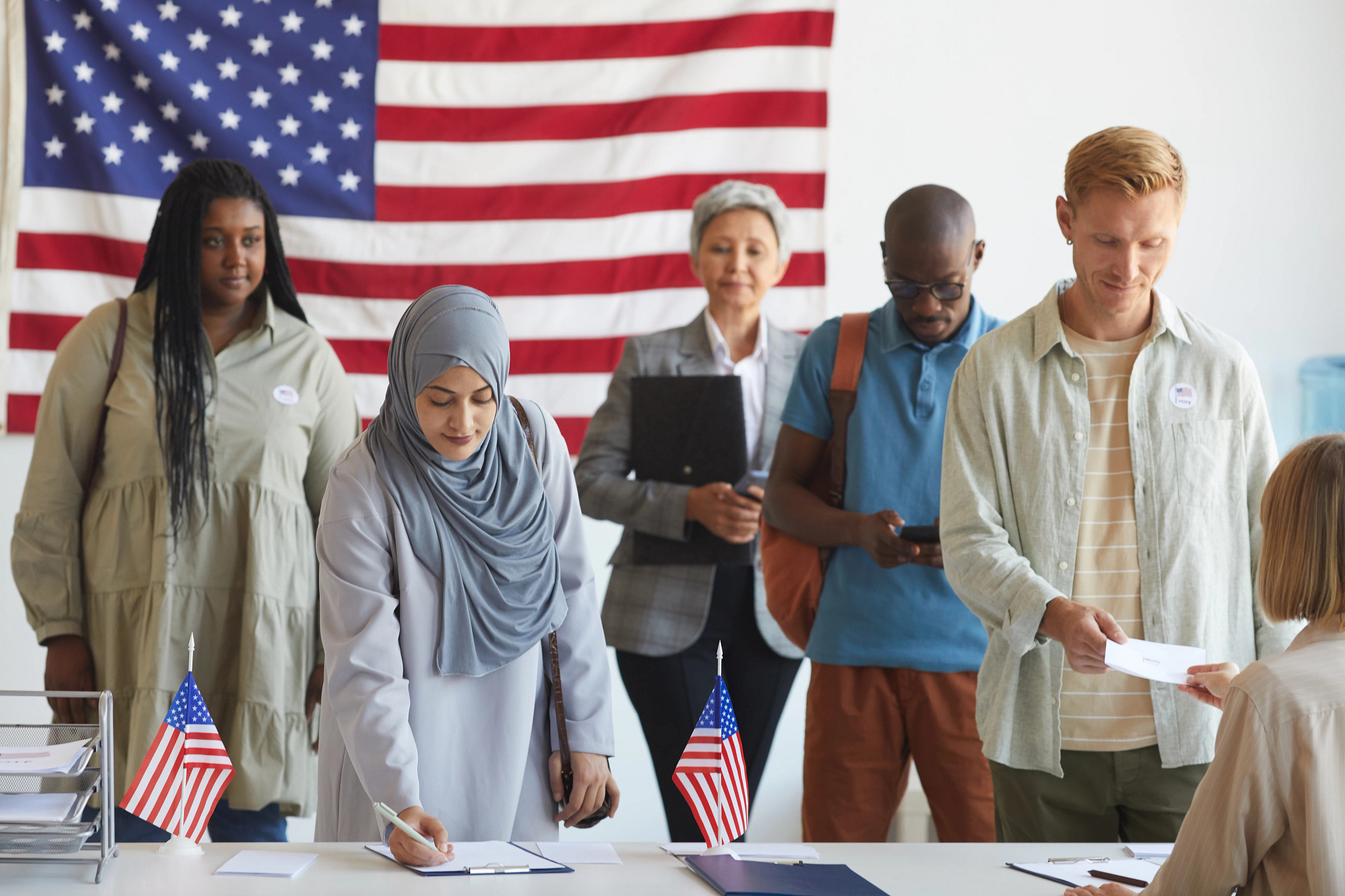 Diverse group preparing to vote with a U.S. flag in the background