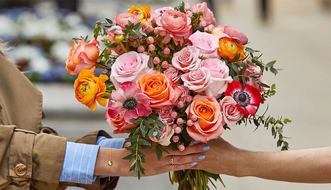Close up of a woman being handed a bouquet of beautiful pink and orange roses and other flowers