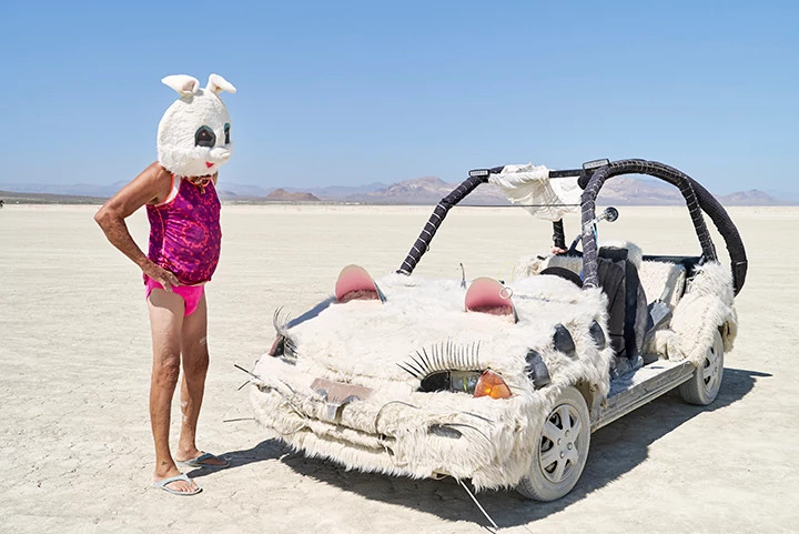 a person wearing a bunny head looking at a car with a cat face and fur