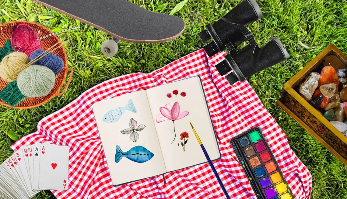 Return to Your Childhood Hobbies a photo collage combines a deck of cards, knitting basket, skateboard, watercolors, binoculars and a sketchbook atop a picnic blanket on grass