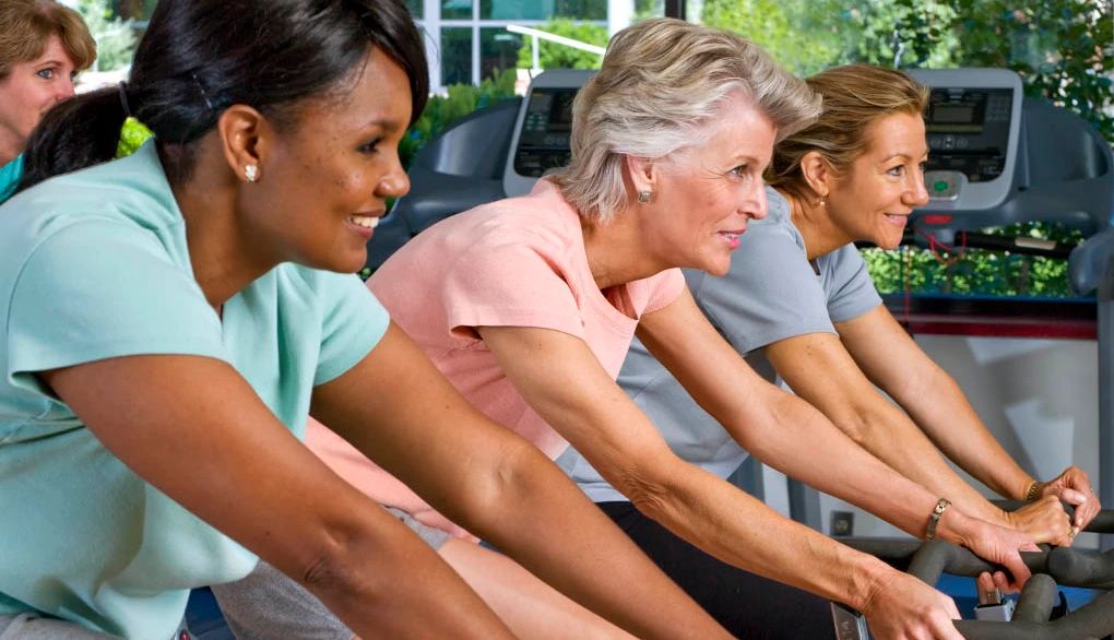 Riding a bike is good exercise for brain health and happiness A group of women on exercise bikes in a gym
