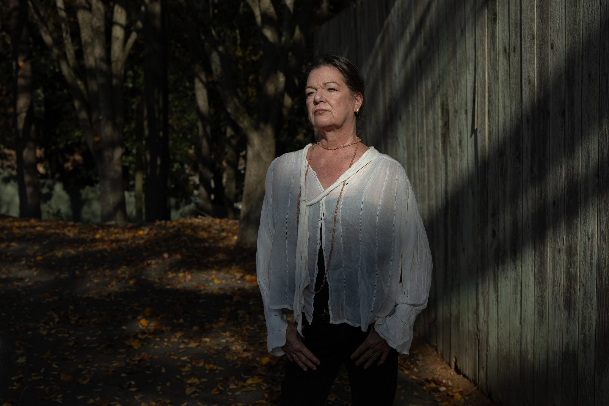 a woman dressed in a white shirt and dark pants stands outside