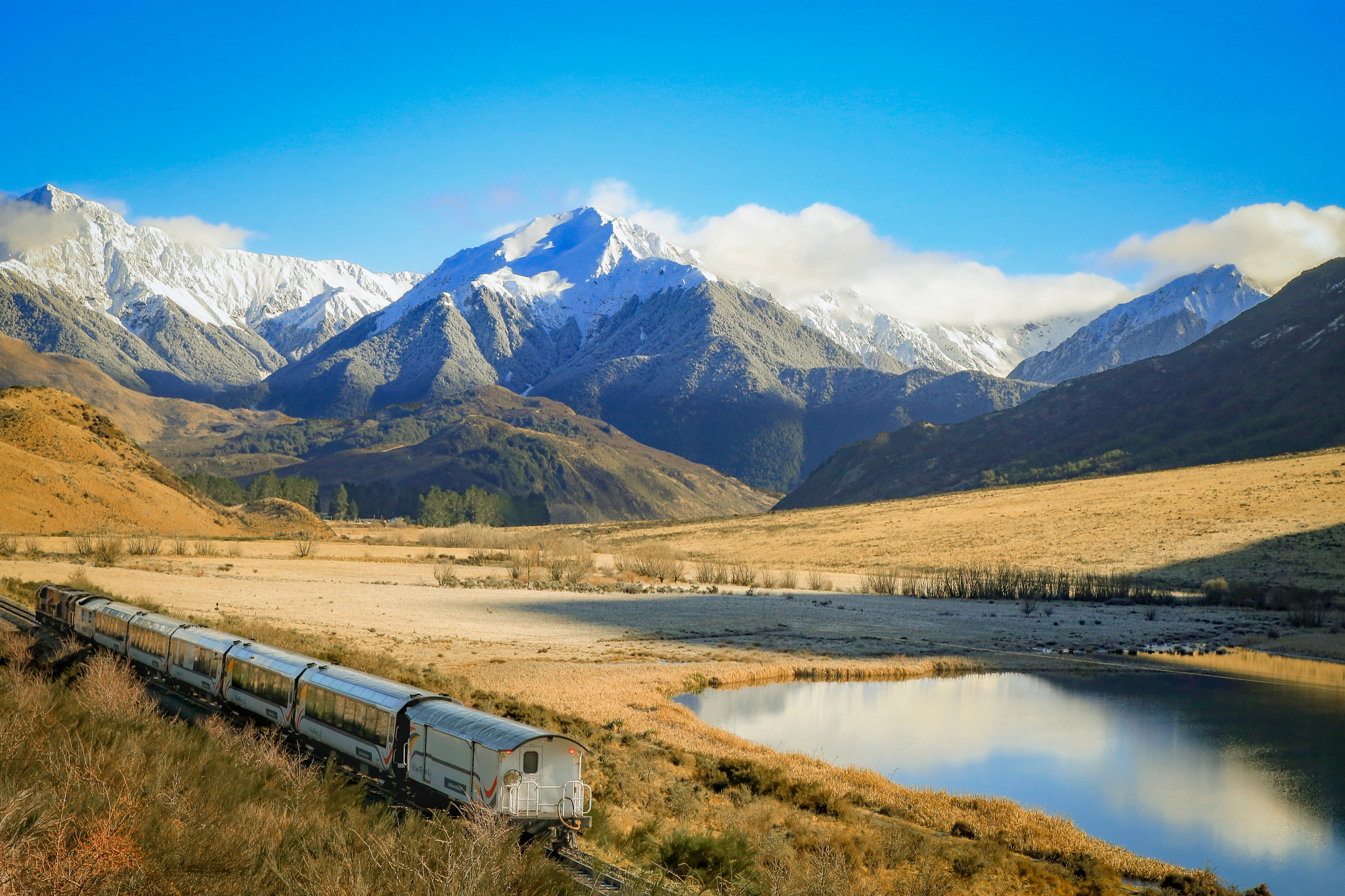 a train traveling near a lake with mountains in the background
