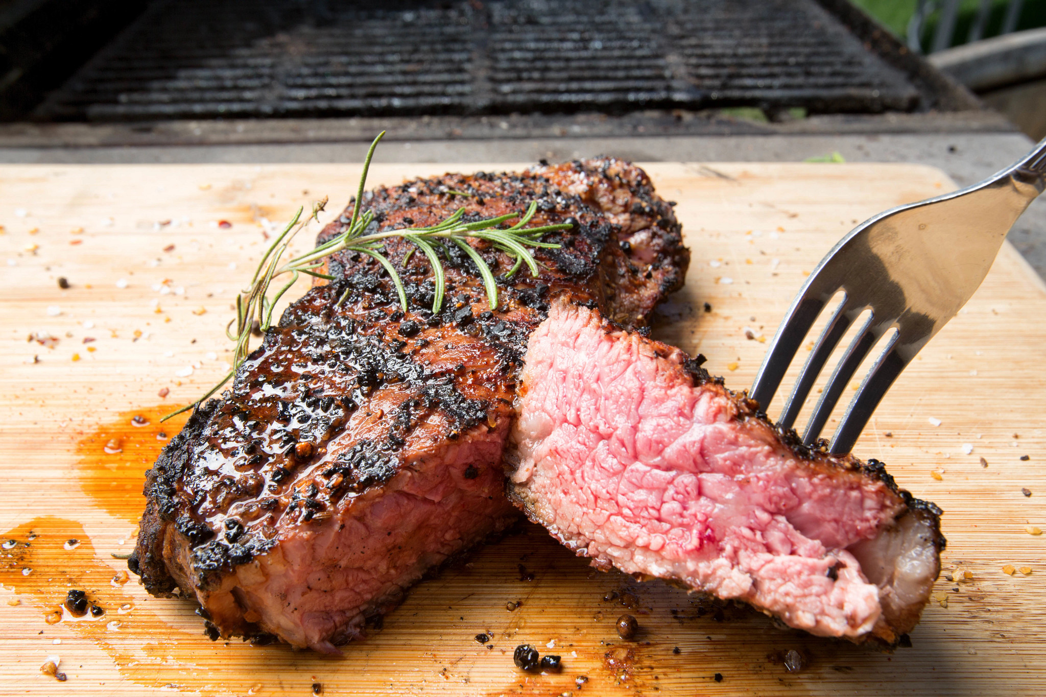 A man cuts into a gorgeous, freshly cooked New York Strip steak, garnished with fresh Rosemary